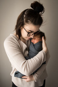 Portrait of hipster millennial mom snuggling swaddled newborn son