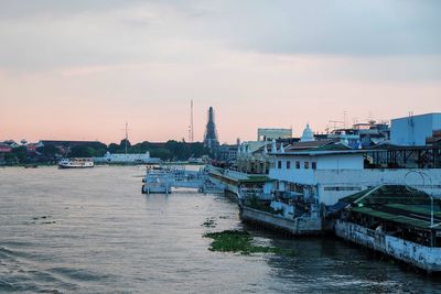 Scenic view of river by buildings against sky during sunset