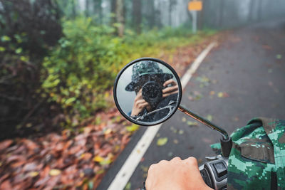 Reflection of man photographing on side-view mirror