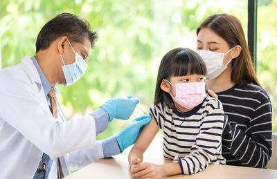 Doctor vaccinating girl sitting with mother
