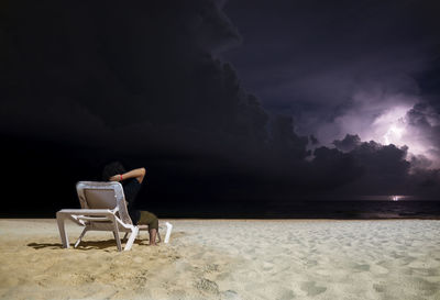 Man sitting on chair at beach against sky