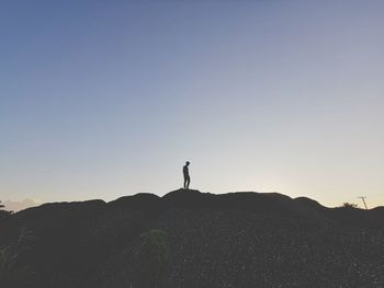 Silhouette person standing on rock against sky during sunset