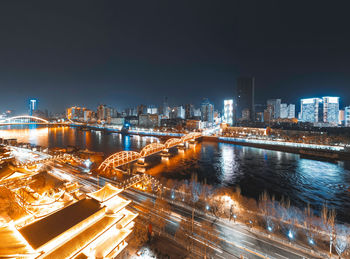 Illuminated city by river against sky at night