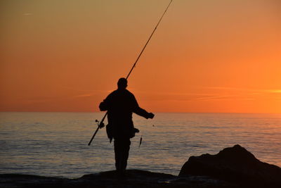 Silhouette man standing on beach against sky during sunset