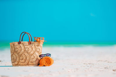 Wicker basket on sand at beach against blue sky