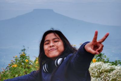 Portrait of smiling girl gesturing peace sign against mountains