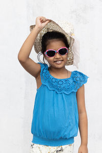 An indian girl wearing sunglasses and holding hat looking at camera with smiling face in summer 