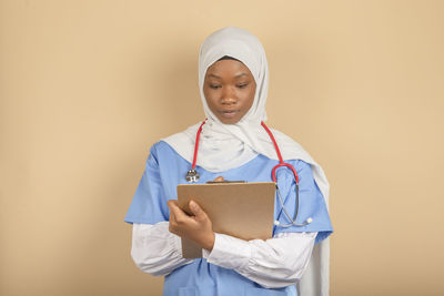 Young woman of muslim religion with white veil holding clipboard and writing something close up.