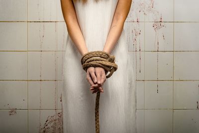 Midsection of woman tied hands standing by wall