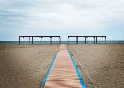 Wooden pier on beach against sky