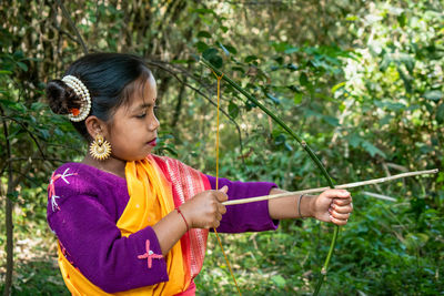 An indigenous indian teenage girl is practicing alone archery in the jungle with a bow and arrow. 