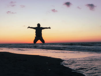 Man jumping at beach against sky during sunset