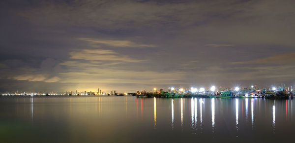 Illuminated city by sea against sky at night
