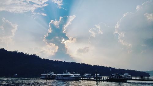 Boats in sea against cloudy sky