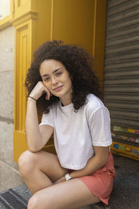 Young woman with curly hair sitting in front of shutter