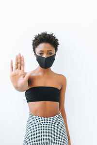 Beautiful young african american woman in black top and face mask isolated on white background