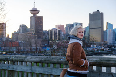 Portrait of young woman standing against buildings in city