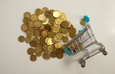 Directly above shot of coins spilling from miniature shopping cart over white background