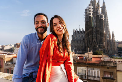 Portrait of smiling young woman standing against buildings