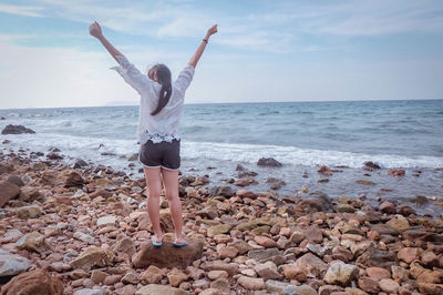 Woman standing on pebbles at beach against sky