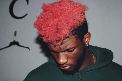 Close-up of young man with red hair looking down while standing against wall