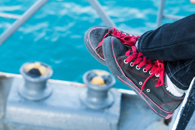 Close-up of person wearing black canvas shoes against blue sea at harbor