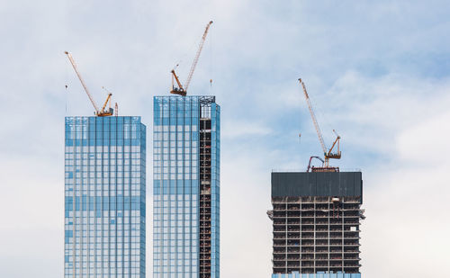 Low angle view of crane by building against sky