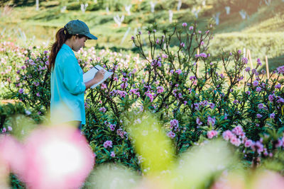 Side view of female researcher examining flowers on land