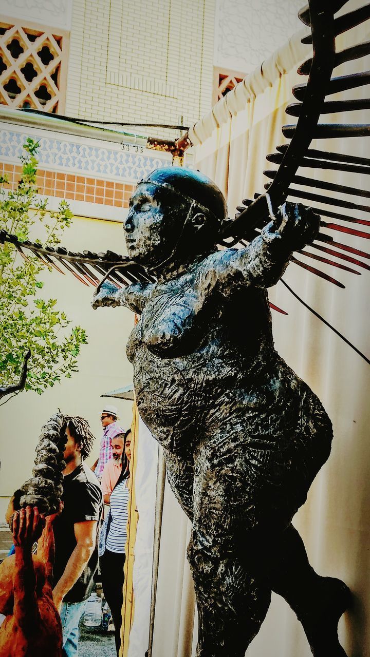 STATUE OF WOMAN STANDING BY SCULPTURE IN CONCERT