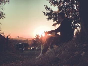 Side view of man sitting on land against sky during sunset