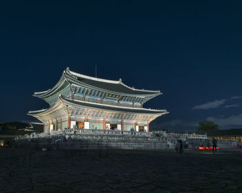 People on illuminated building against sky at night