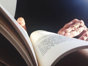Close-up of hand holding book against black background