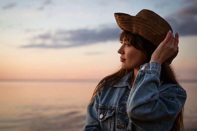 Woman standing by sea against sky during sunset