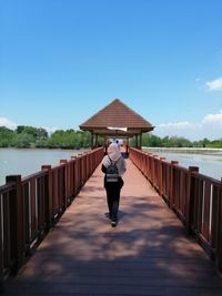 Rear view of man standing on railing by lake against sky