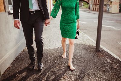Low section of couple holding hands walking on footpath
