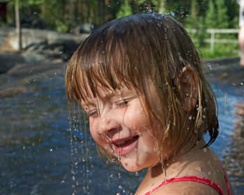 Close-up of water splashing on girl smiling by river