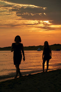 Silhouette couple walking at beach during sunset