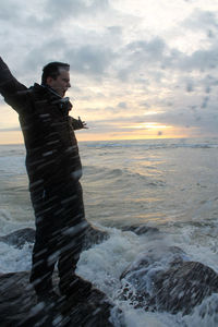 Full length of man with arms outstretched standing on rock by sea