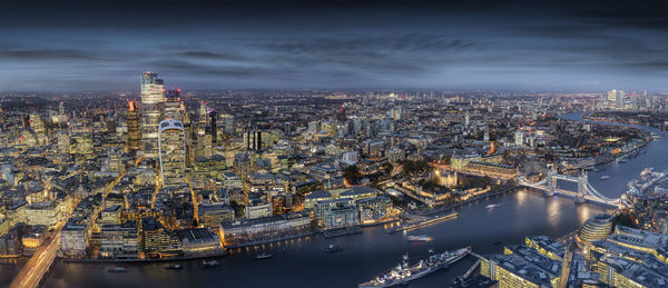 Aerial view of illuminated city by river against sky during dusk