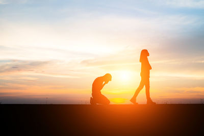 Silhouette man and woman against sky during sunset