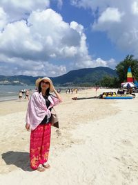 Portrait of woman standing at beach against cloudy sky