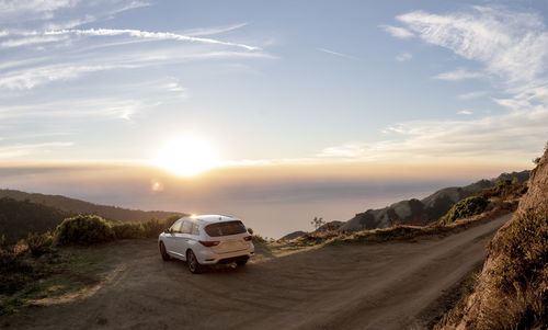 Cars on road by land against sky during sunset