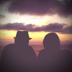 Silhouette people sitting by sea against sky during sunset