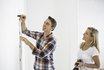 Man measuring white wall while standing by girlfriend at home