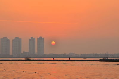 Scenic view of sea by buildings against sky during sunset