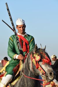 Portrait of man wearing traditional clothing riding horse against clear sky