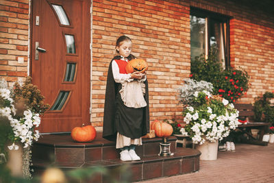 Full length of cute girl holding pumpkin standing against house