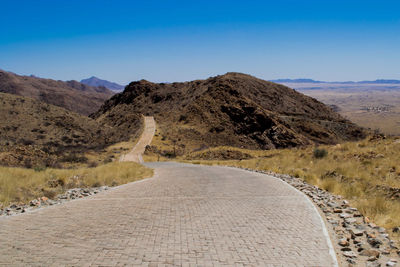 Road leading towards mountain against blue sky