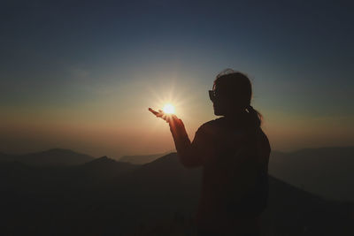 Silhouette woman gesturing by sun against sky during sunset