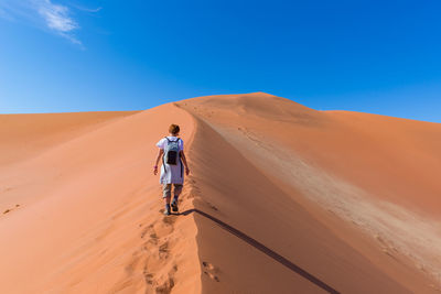 Rear view of man in desert against blue sky